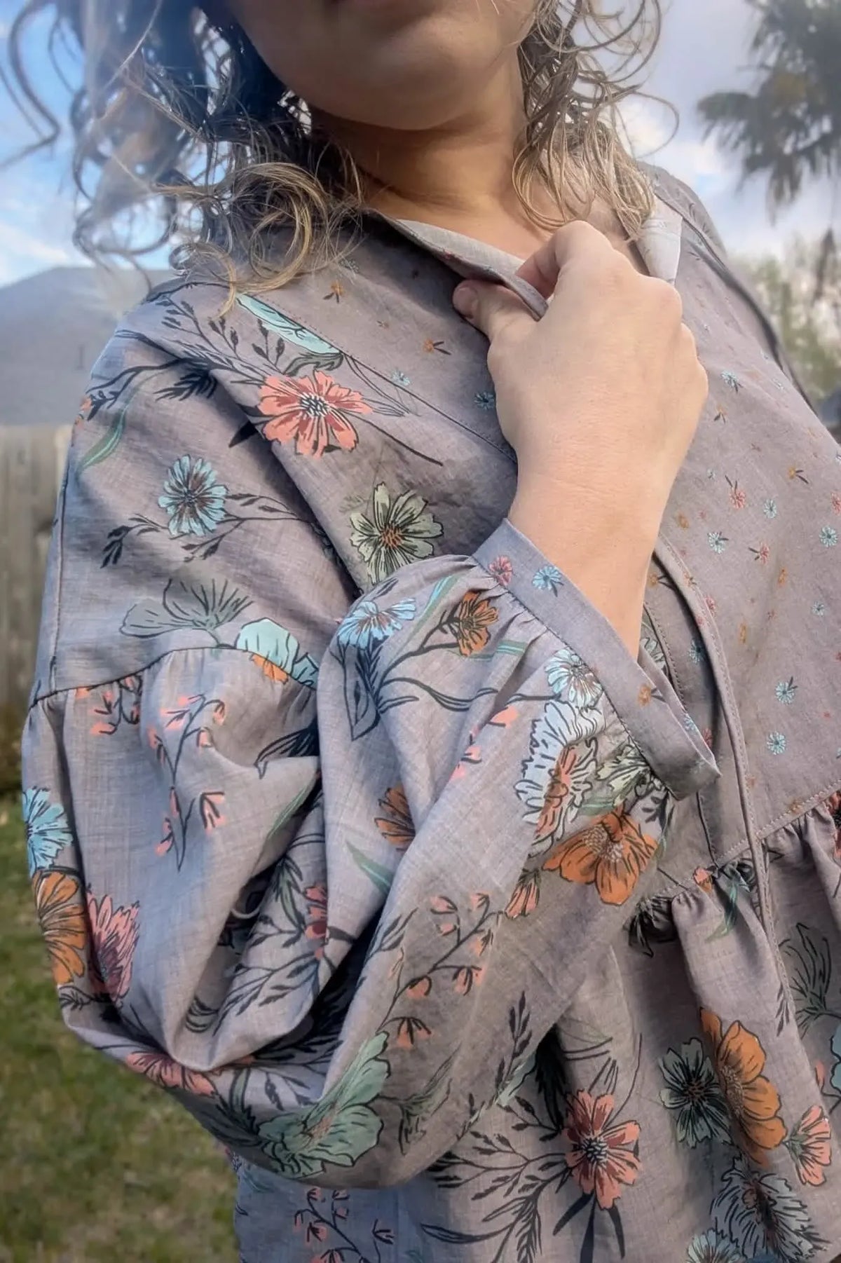 A person wearing a taupe floral print top with ruffled sleeves.
