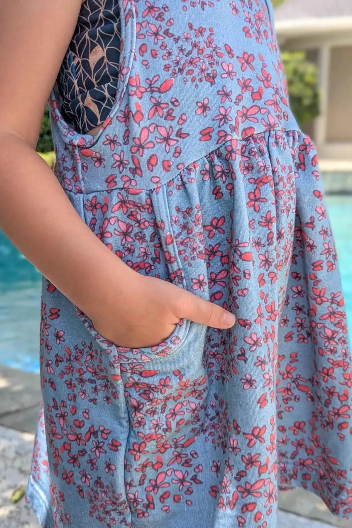 A child's arm and hand in the pocket of a blue floral dress.