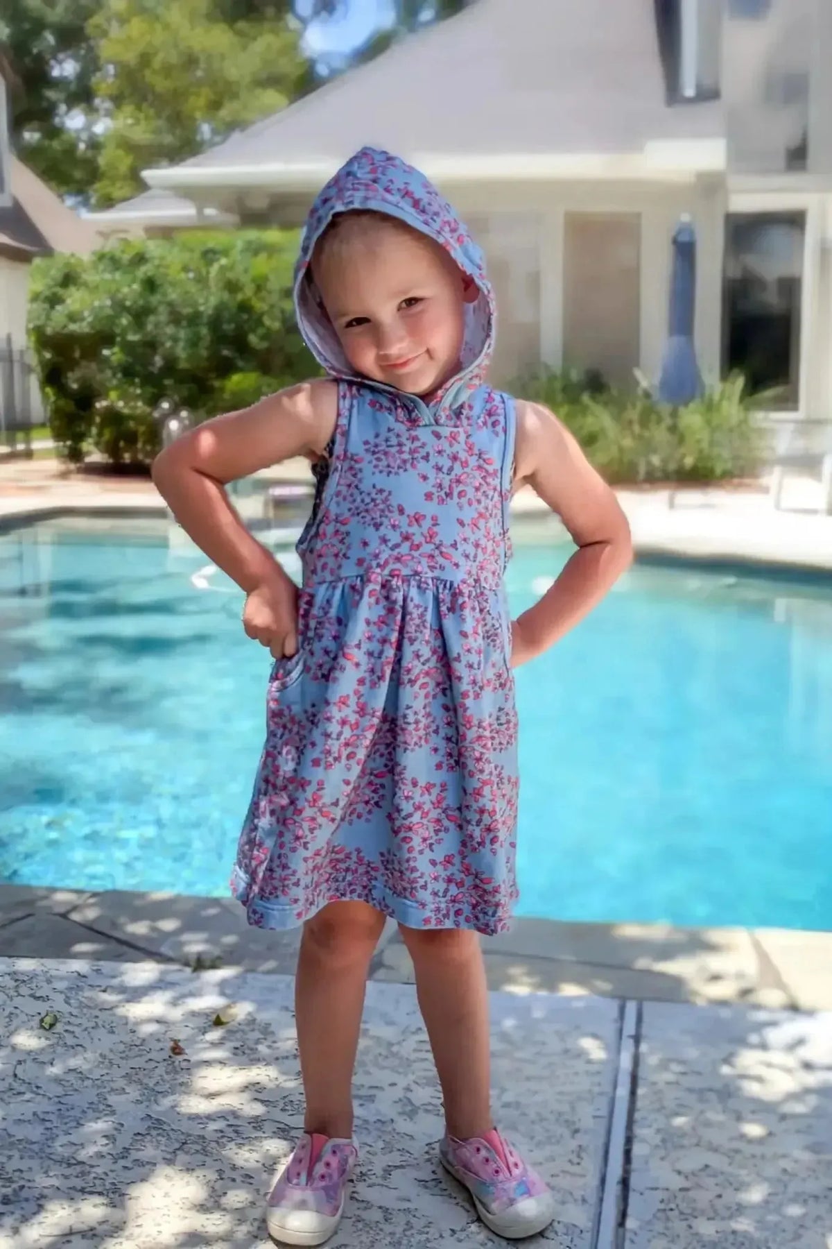 Light blue fabric with red floral pattern, shown as a child's sleeveless hooded dress.