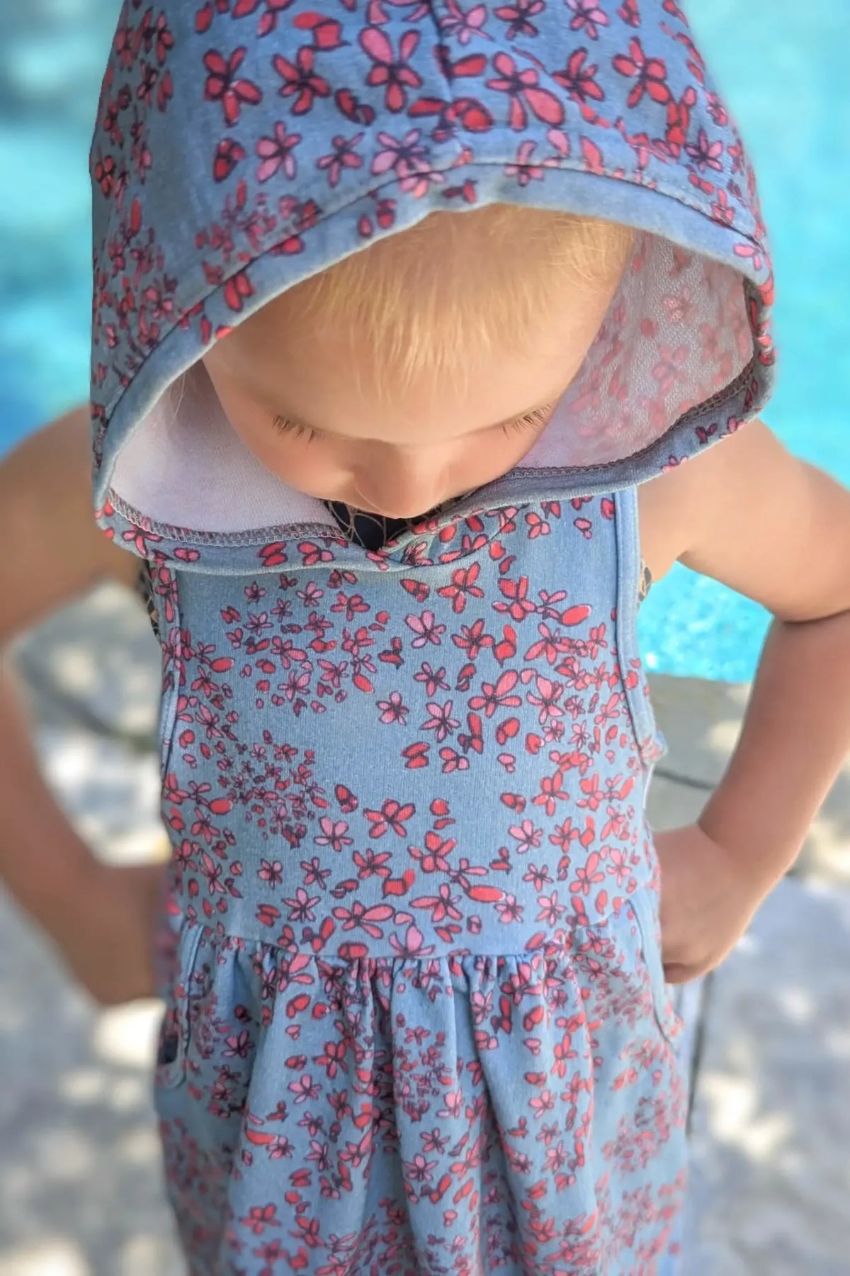 A child in a blue floral hooded dress looks down.