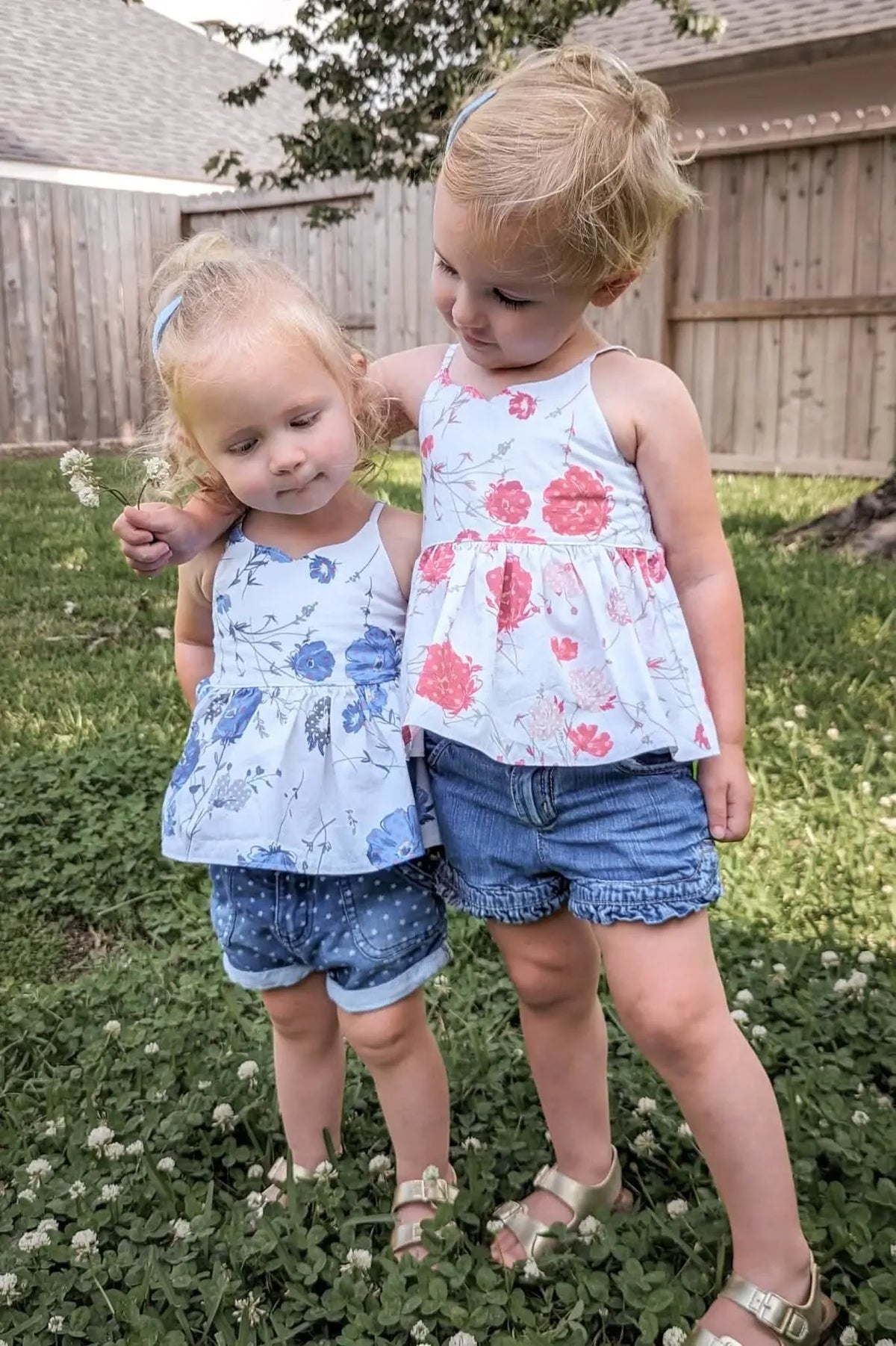 Two young girls wear floral tops, one with red blooms and the other with blue.