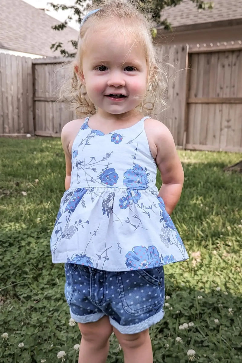 A young girl wears a white top with blue floral patterns and star-print denim shorts.
