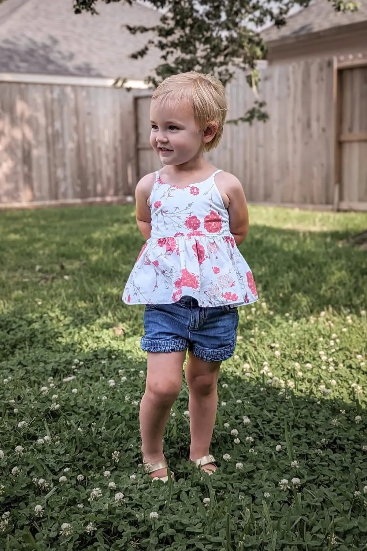 A young child wears a top with a red floral pattern and blue shorts.