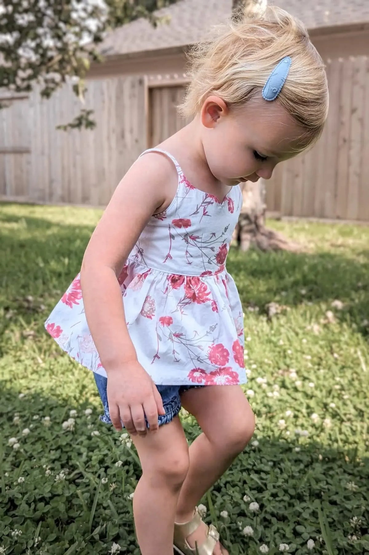 A young girl in a white floral top with red blooms and denim shorts.