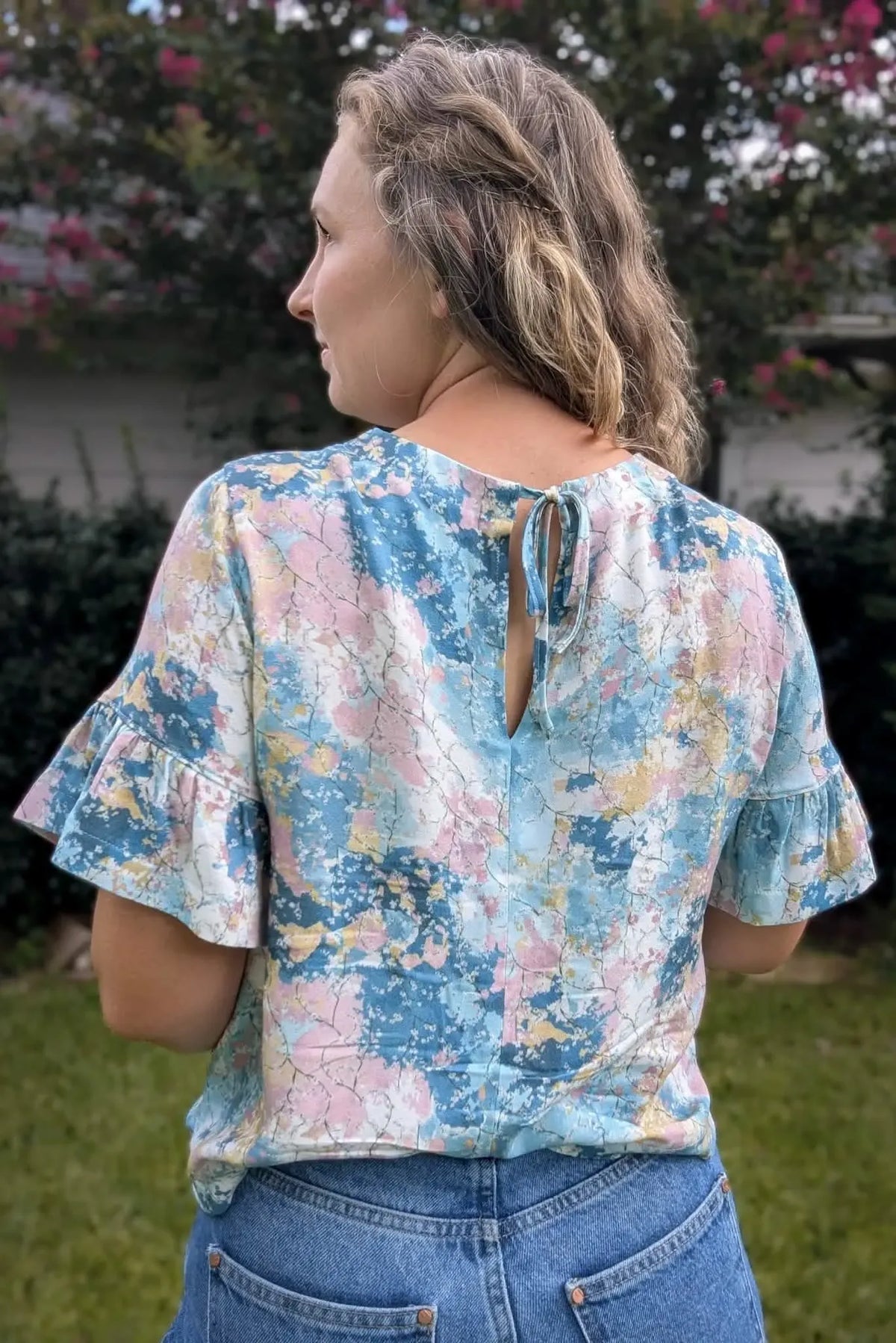 A woman from behind wears a blue, pink, and white patterned top with ruffled sleeves.