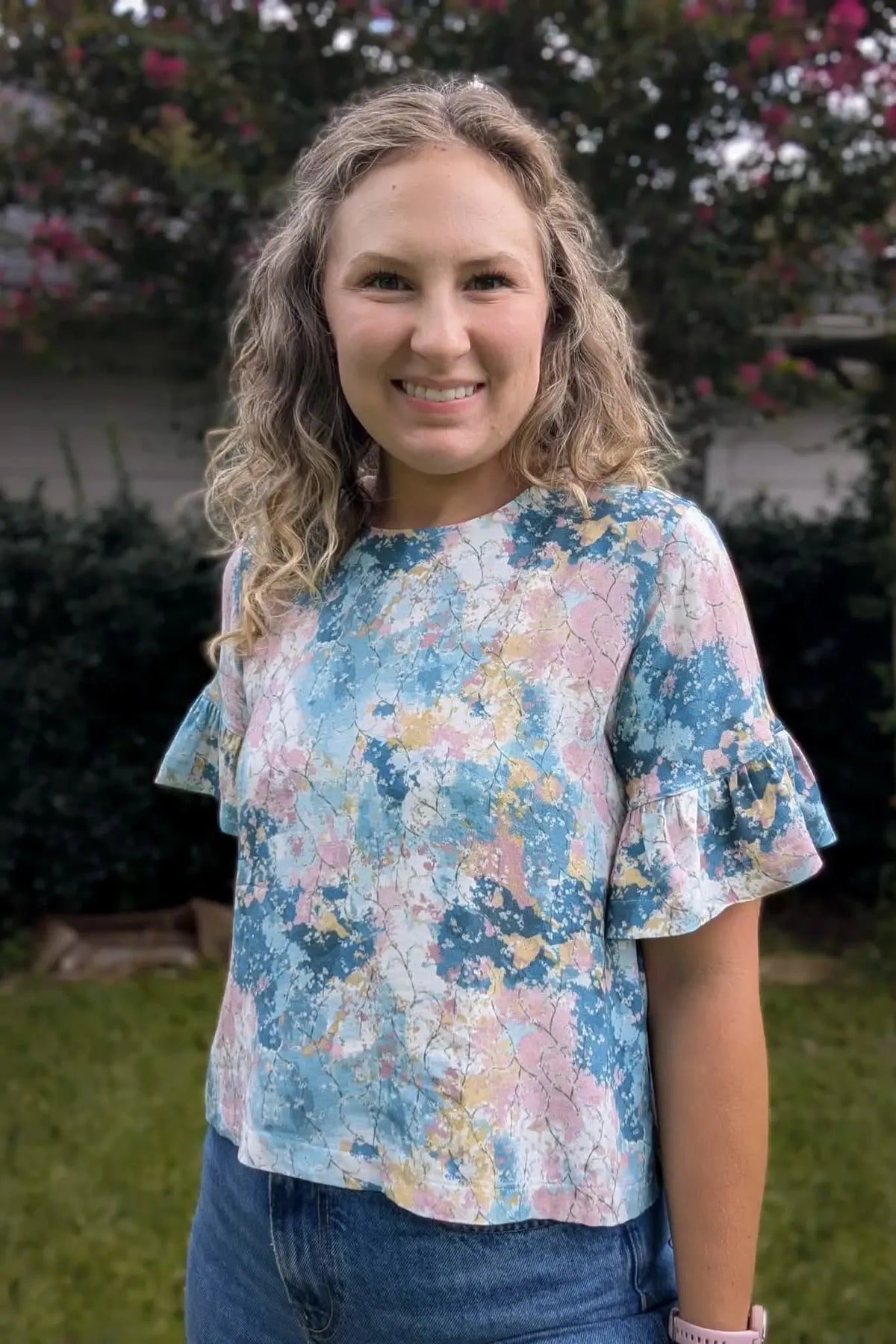A woman wears a floral top with ruffled sleeves and blue jeans.