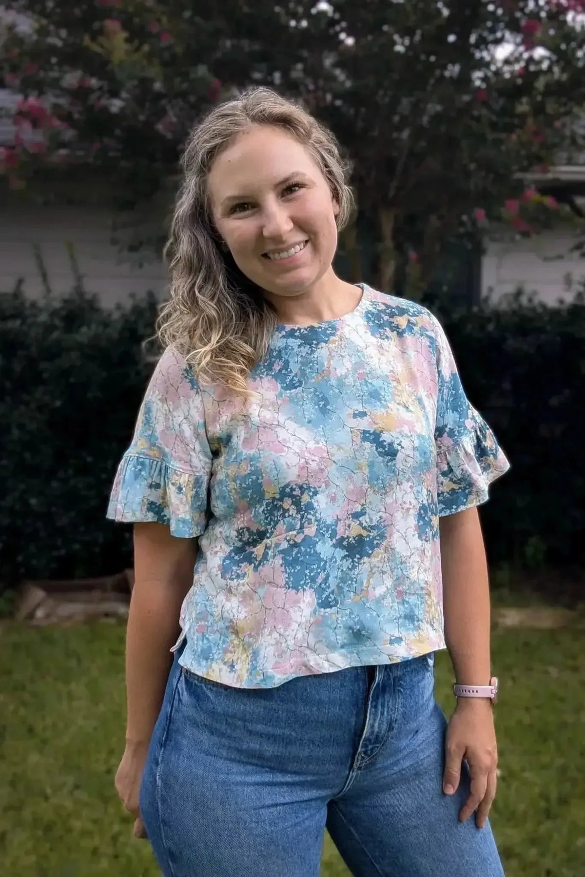 Woman wearing a blue and pink abstract floral print blouse with bell sleeves outdoors.