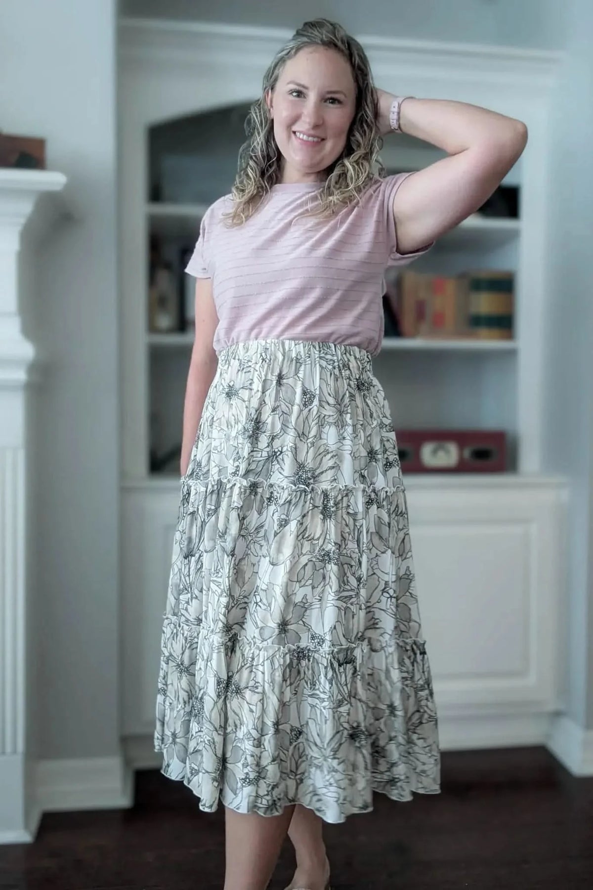 A woman wears a pink striped top and a tiered skirt with a sepia floral sketch pattern.