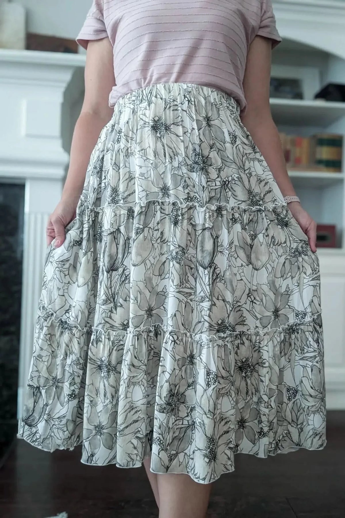 A person wears a tiered maxi skirt with a sepia floral sketch pattern.