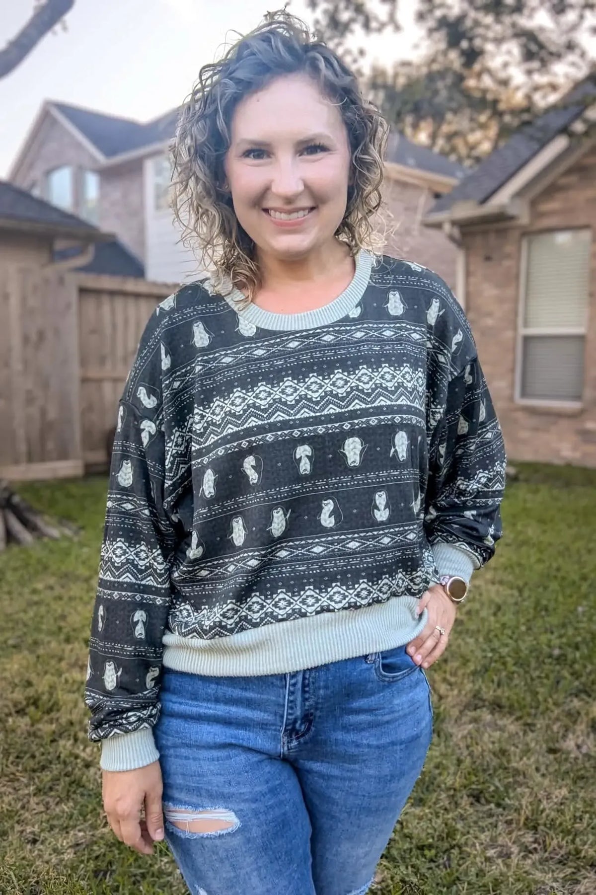 A woman smiles wearing a dark gray sweater with white penguin and geometric patterns.