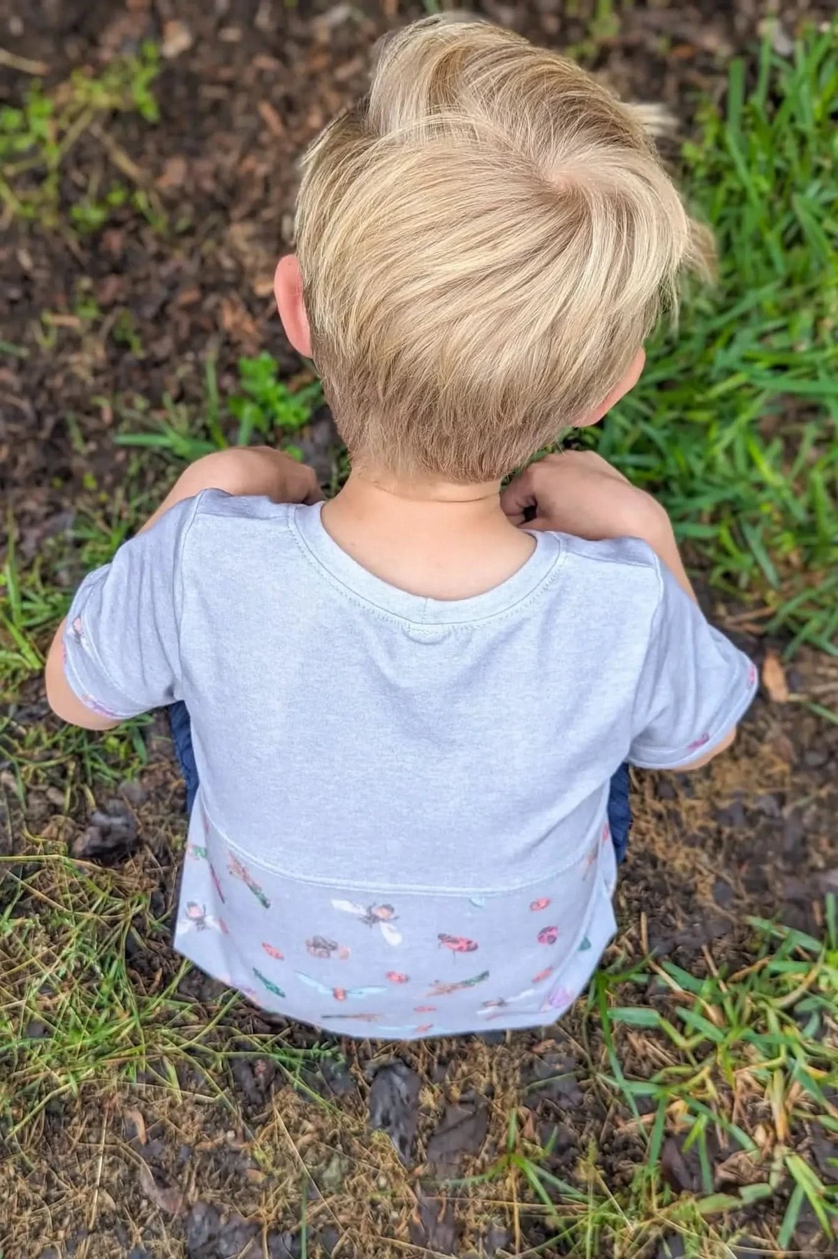 Child from behind wearing a light gray shirt with a colorful bug pattern.