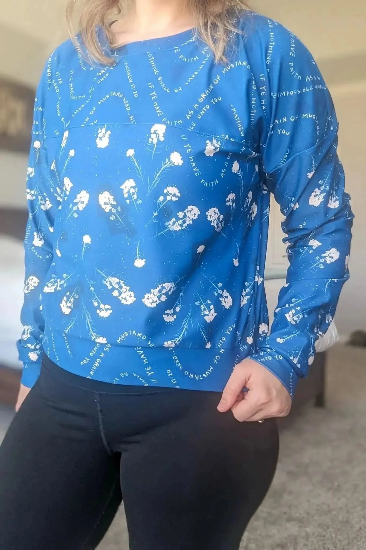 A person wears a blue long-sleeved shirt with white flowers and text.