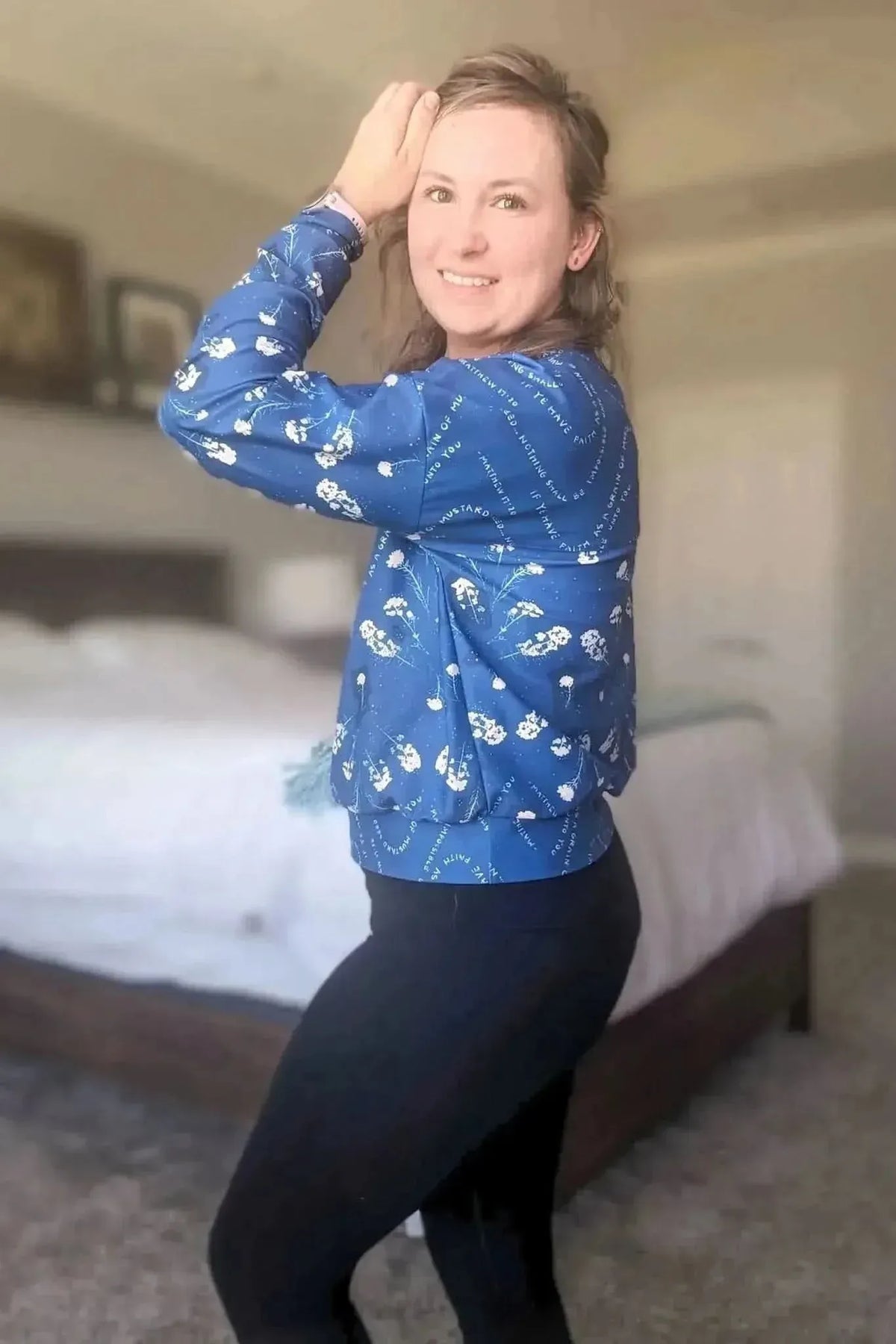 Woman wearing a blue long-sleeved top with white floral and text print.