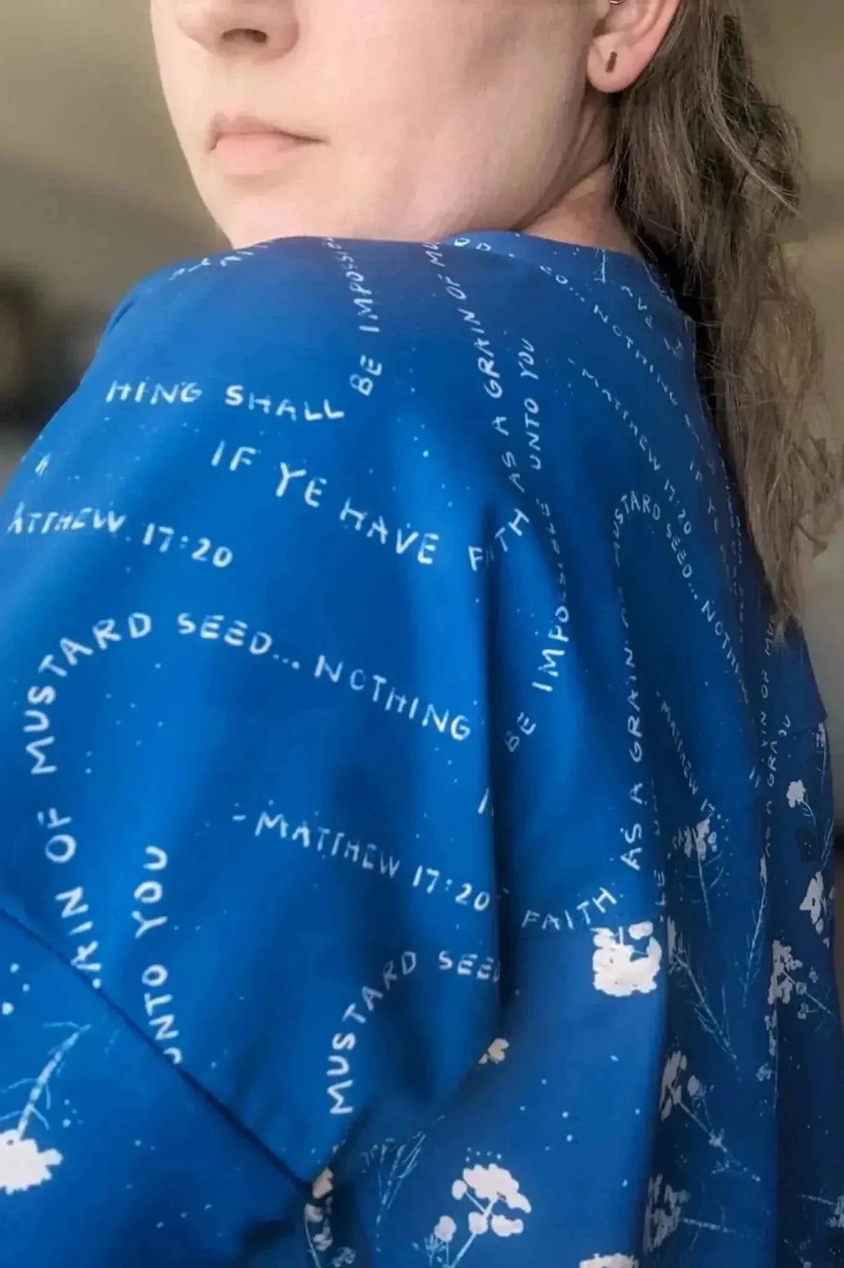 A person wears a blue fabric with white text and floral designs.