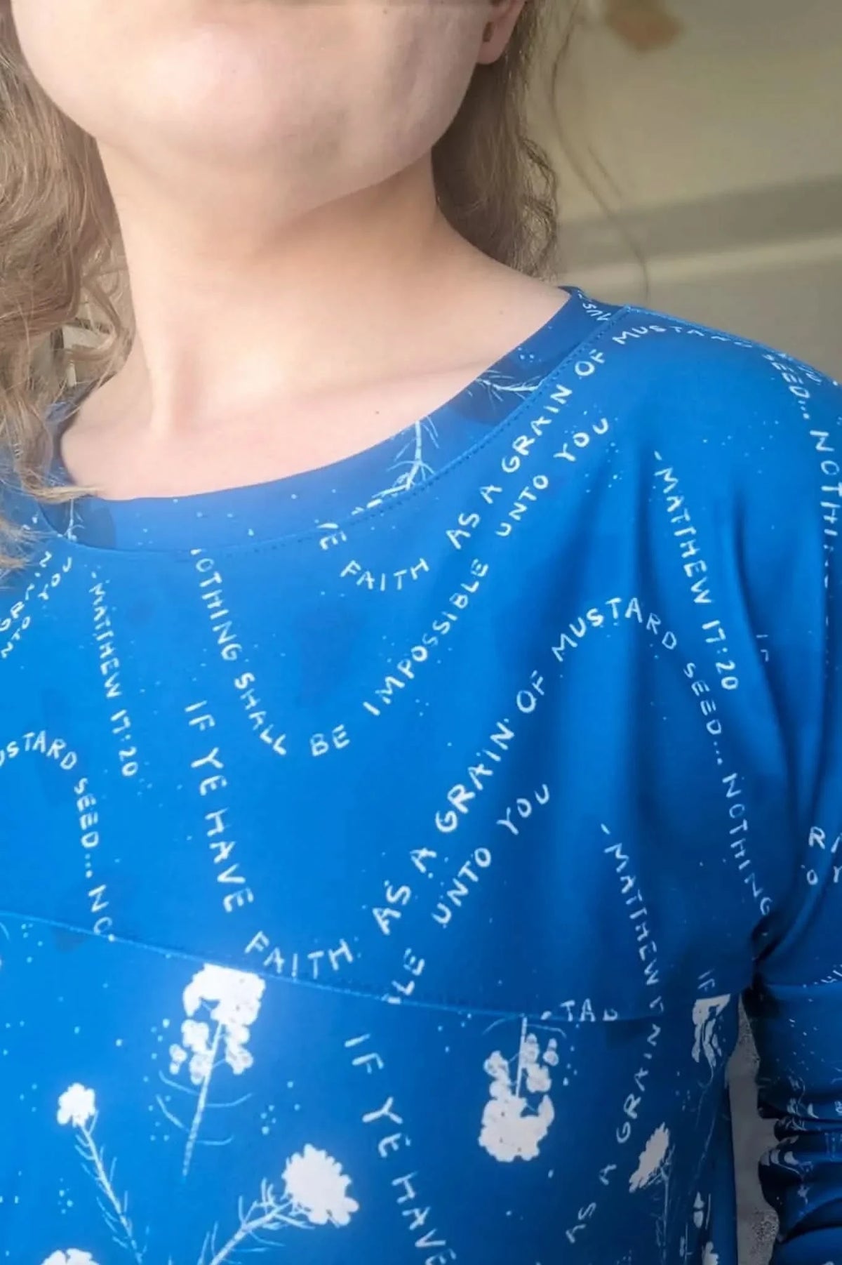 A woman wears a blue top with white text and floral designs.