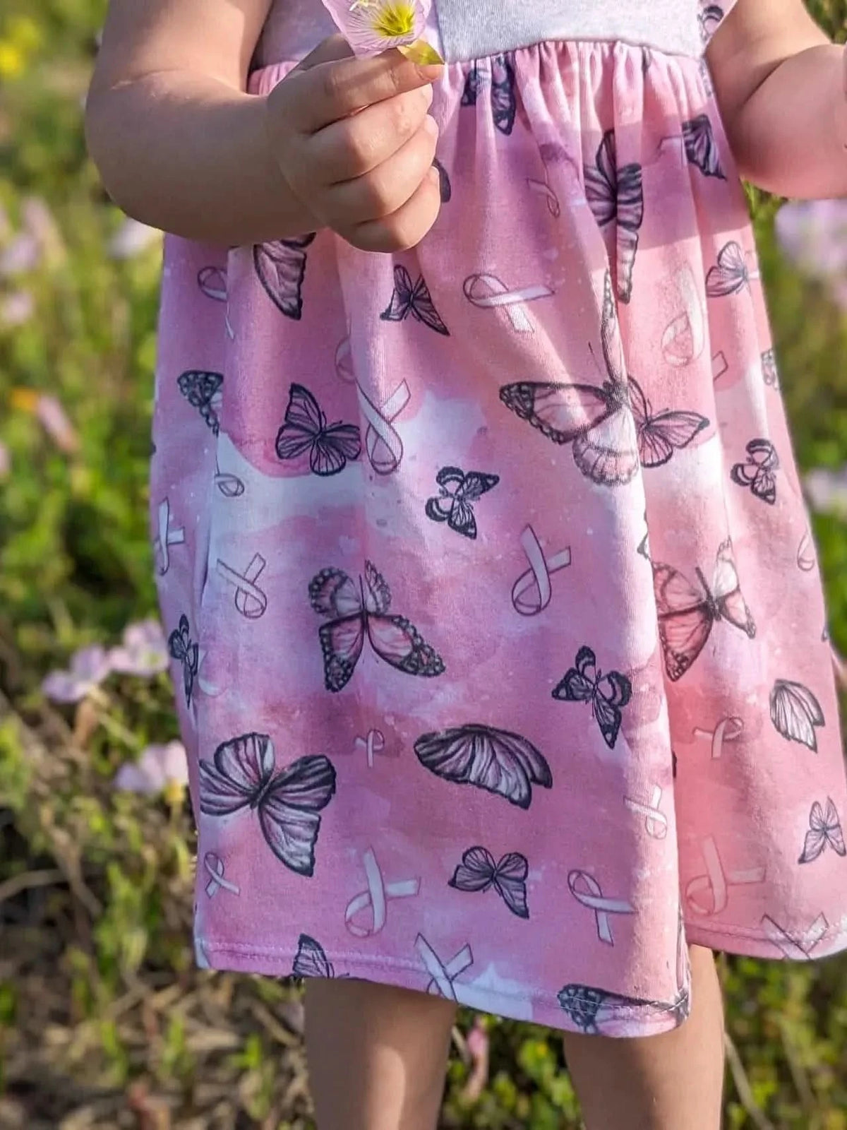 A child in a pink dress with butterflies and breast cancer ribbons.
