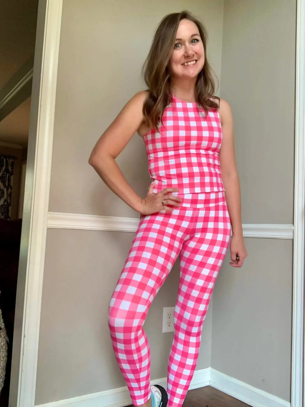 A woman smiles, wearing a hot pink and white gingham tank top and matching leggings.