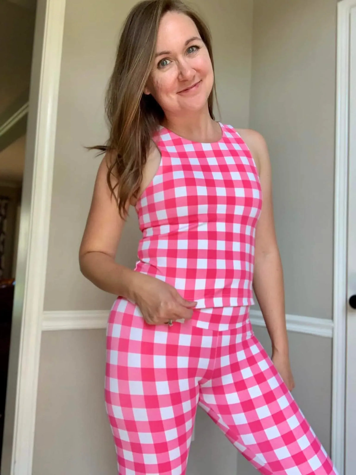 A woman wears a hot pink and white gingham tank top and matching leggings.
