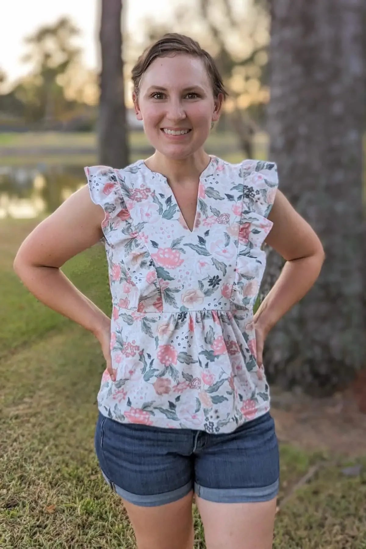 A woman wears a floral top with blush flowers and green leaves.