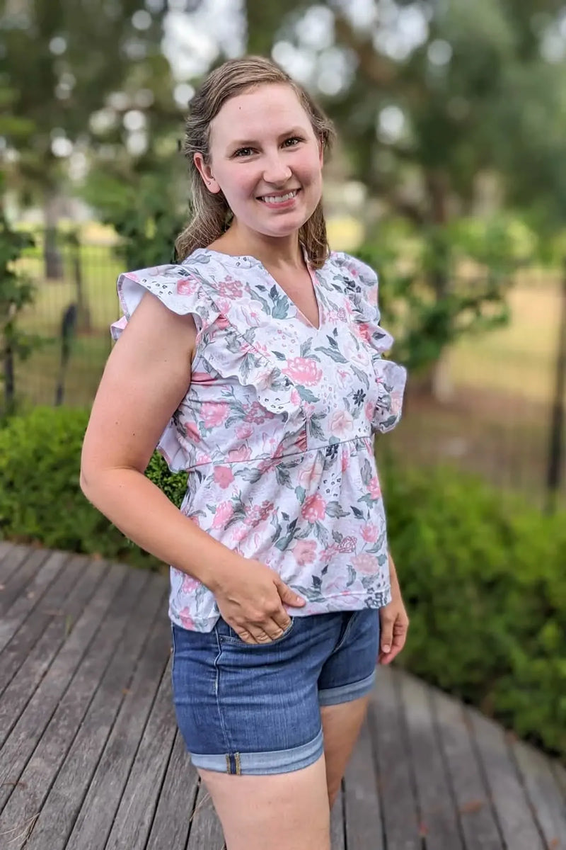 A woman wears a floral top with ruffles and denim shorts.