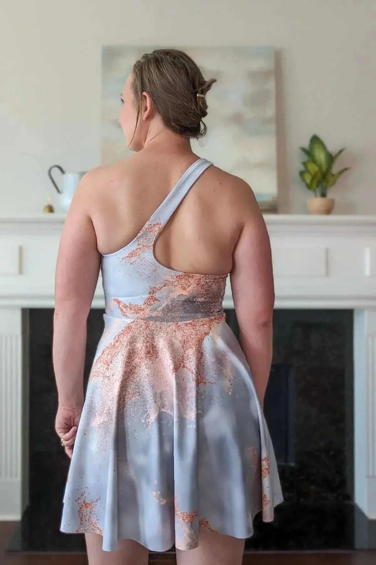 A woman from behind wearing a light blue and rose gold patterned dress.