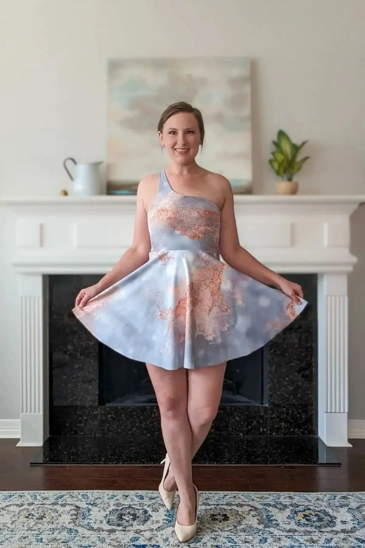 A woman models a one-shoulder dress with a gray and copper abstract pattern.