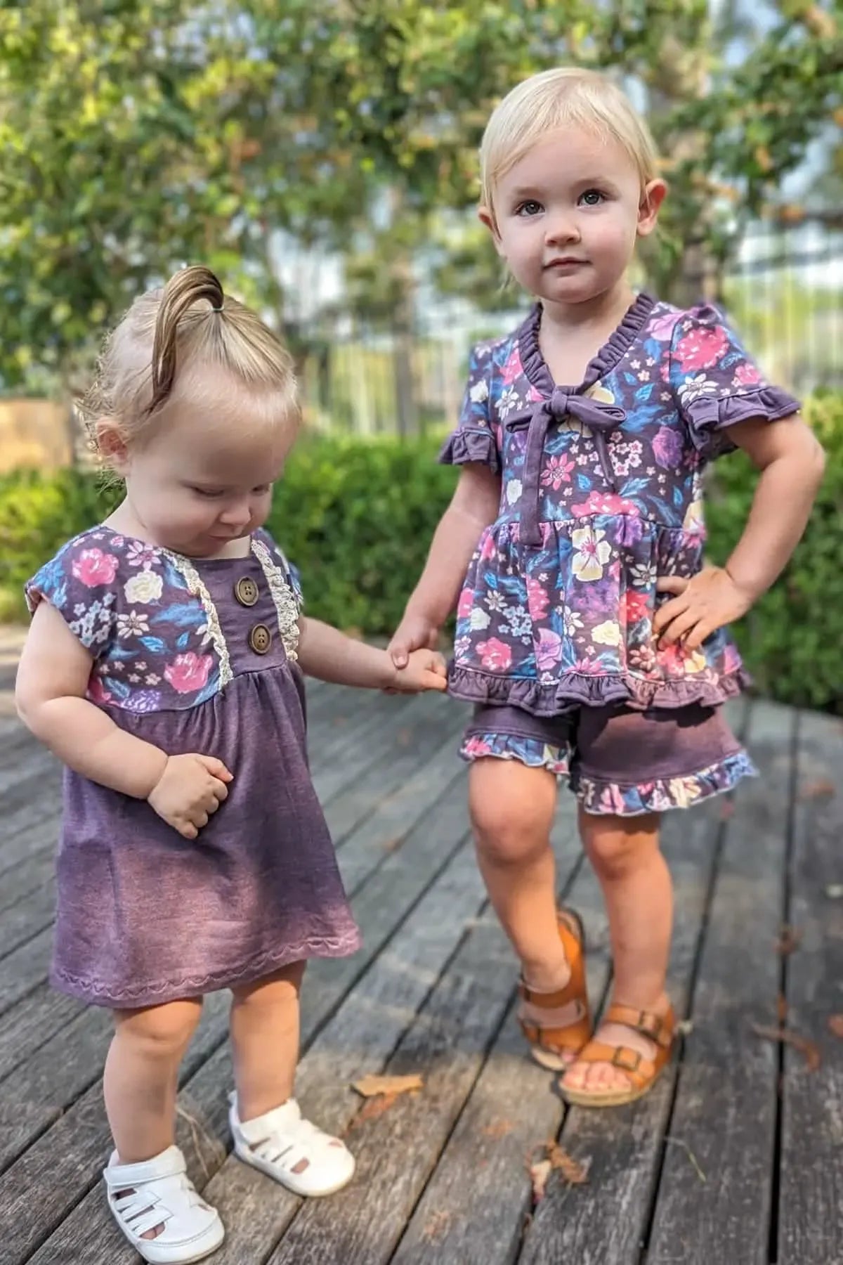 Two young girls wear matching maroon heather outfits with floral patterns.