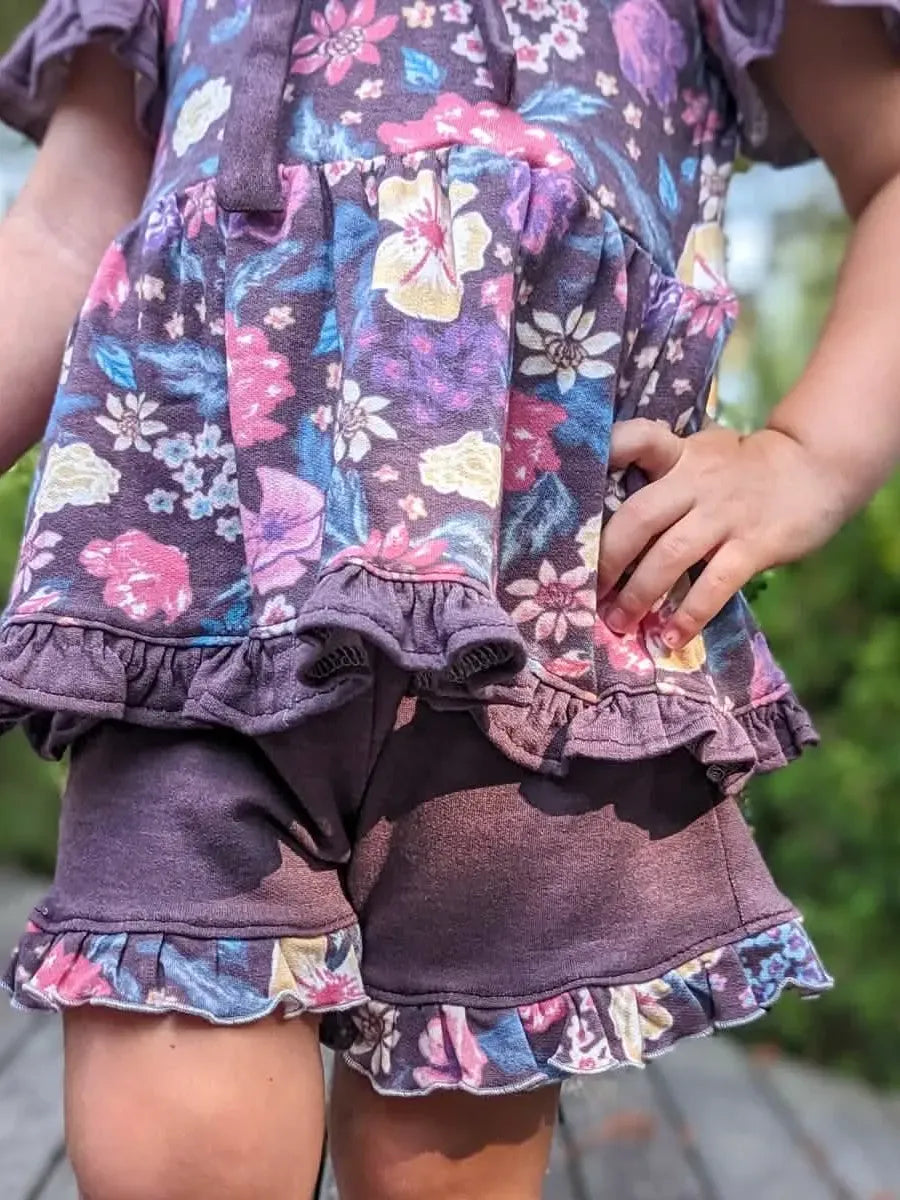 Child in a maroon floral top and shorts with ruffled trim.