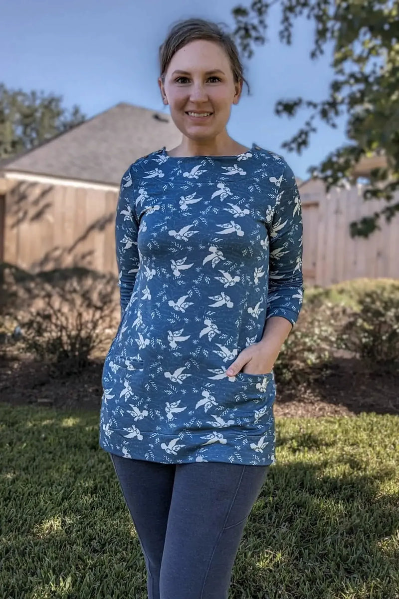 Woman in a blue long-sleeve tunic with white dove print and dark leggings.