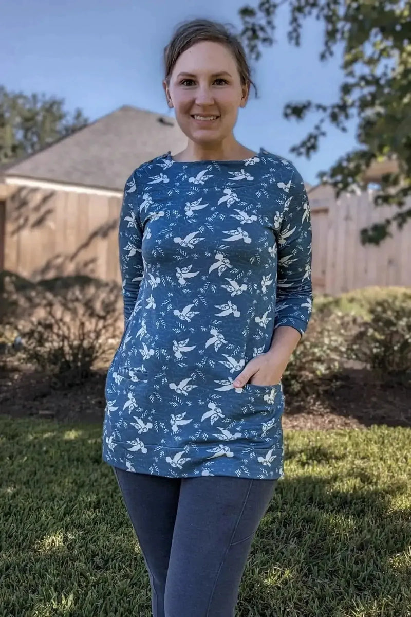 Woman wearing a blue long-sleeve tunic with a white dove pattern and pockets.