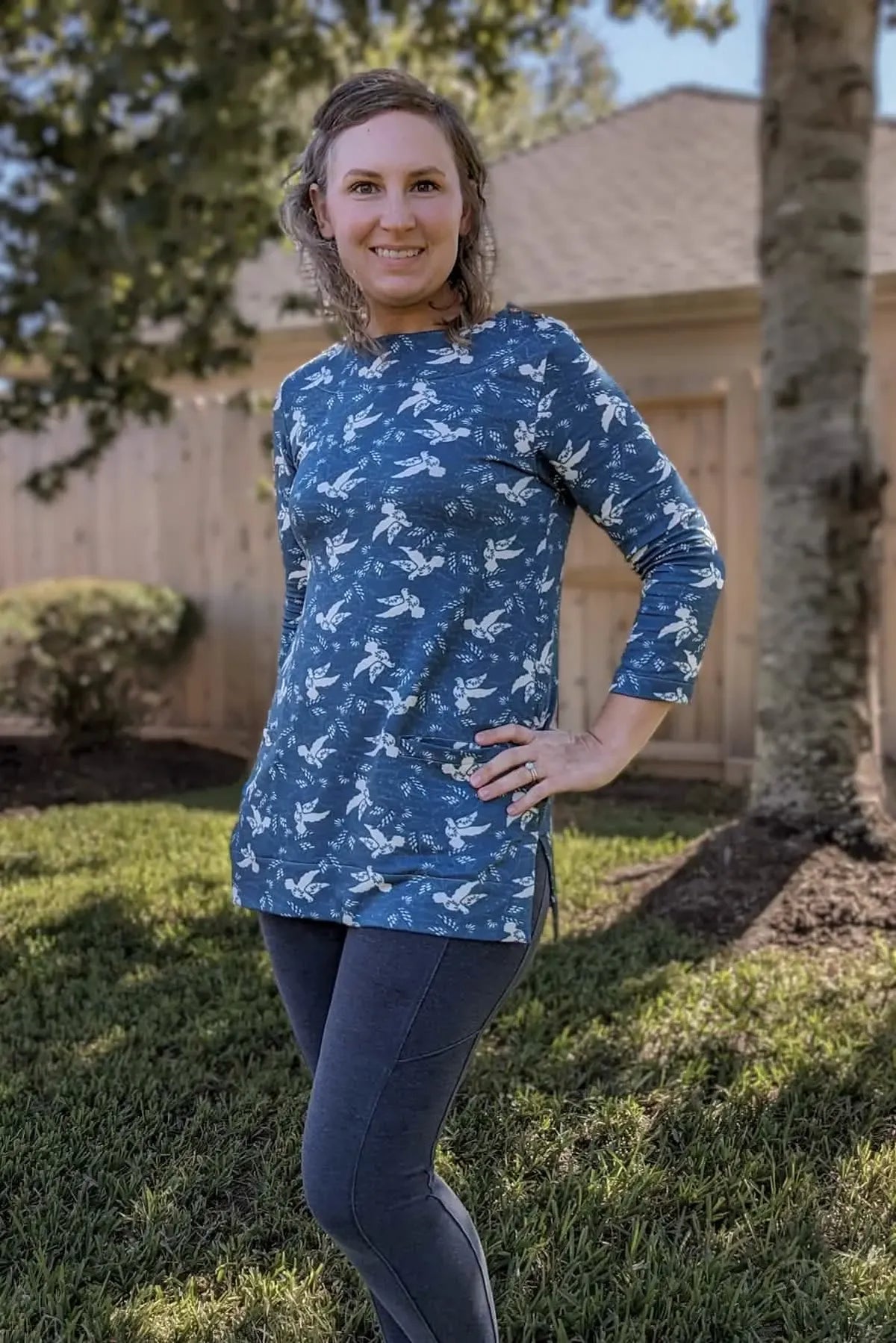 A woman models a blue long-sleeved top with a white dove pattern and dark leggings.