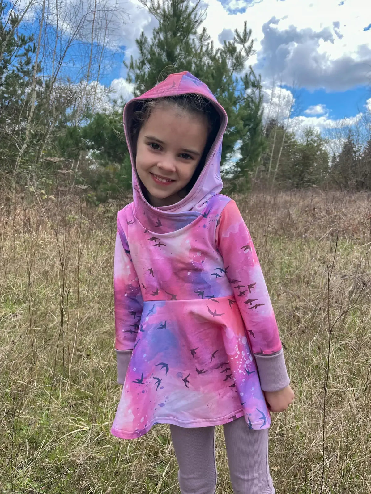 A young girl smiles in a pink and purple hooded dress with bird silhouettes.