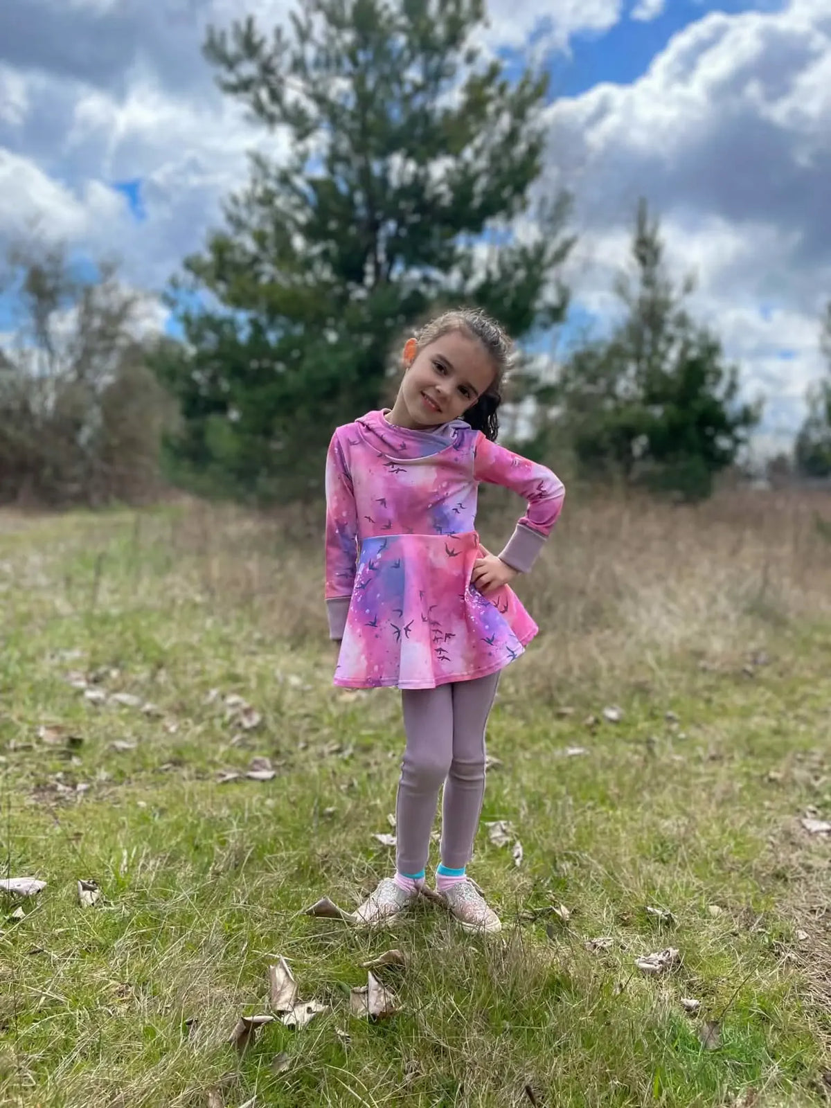 A young girl wears a purple and pink dress with a bird pattern and purple leggings.