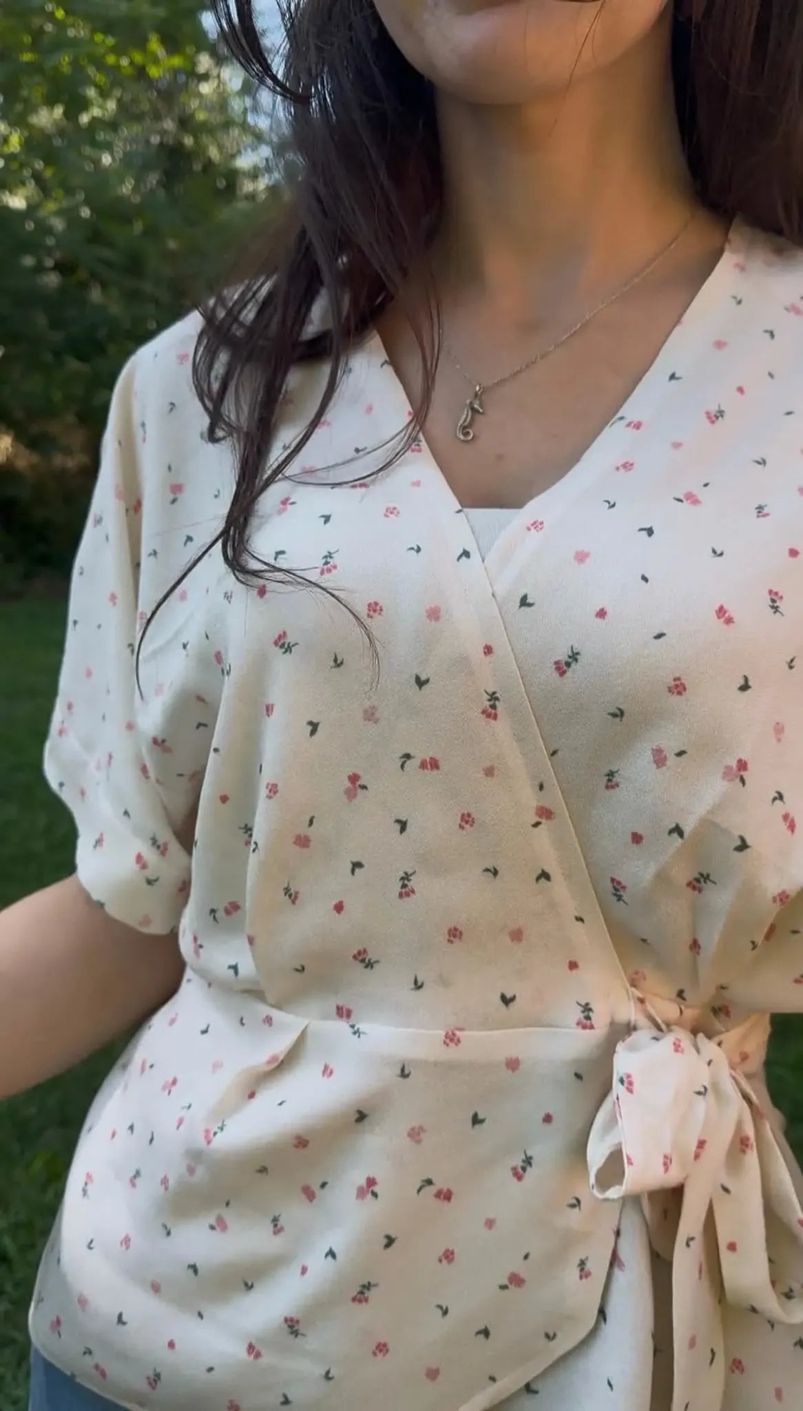 A woman wears a cream-colored wrap dress with small red and green floral patterns.