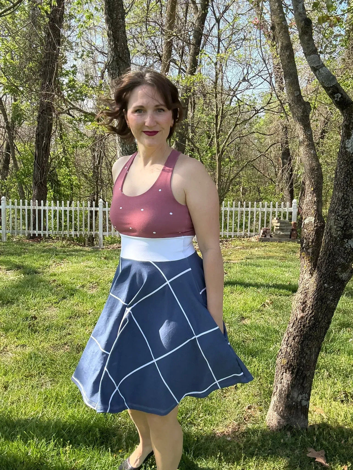 A woman wears a navy windowpane skirt and a polka dot top in a sunny yard.