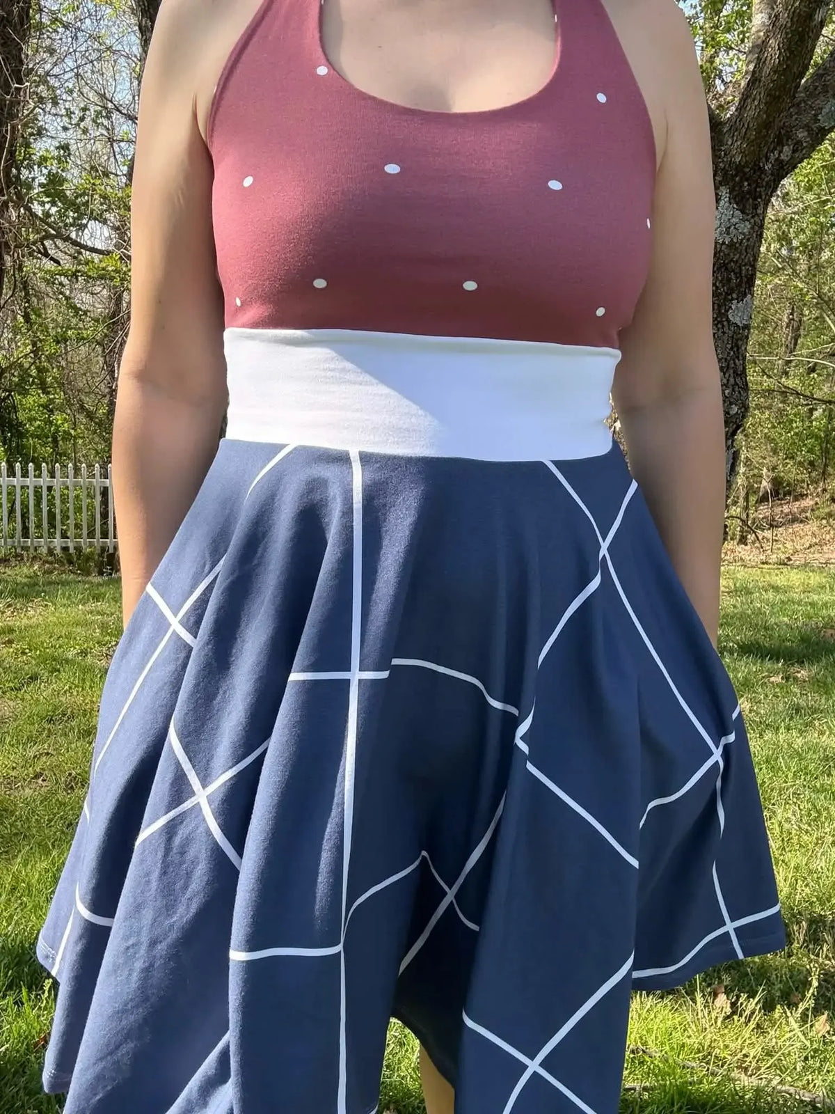 A person wears a navy windowpane skirt and a polka dot top outdoors.