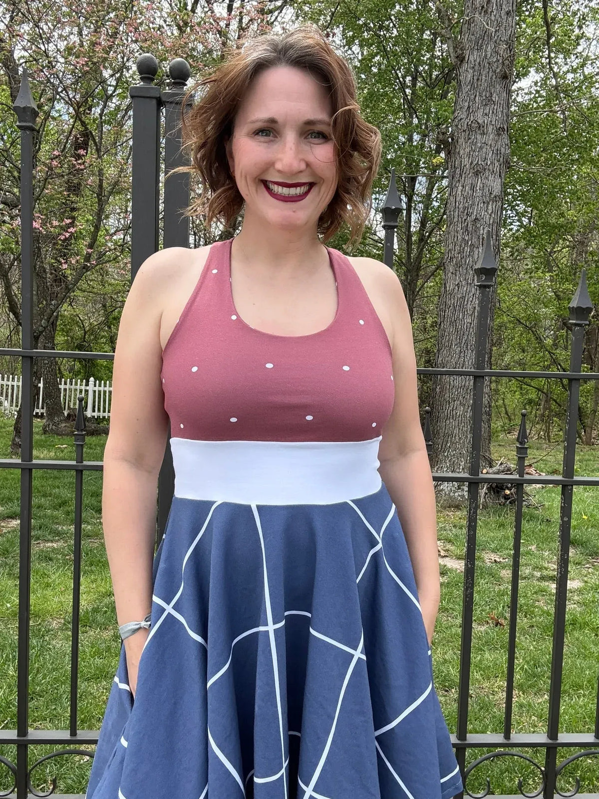 A woman smiles, wearing a dress with a polka-dot top and a navy windowpane skirt.