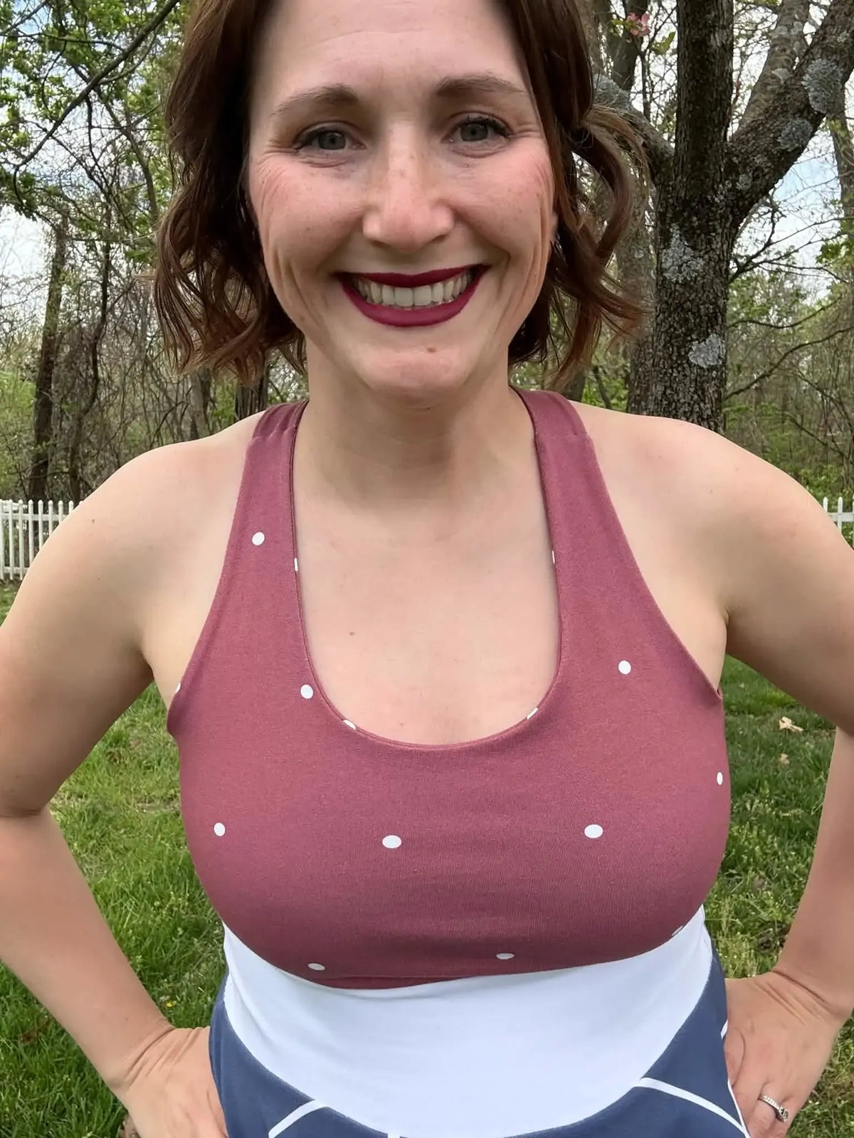 A woman smiles, wearing a red polka dot tank top and blue and white bottoms.