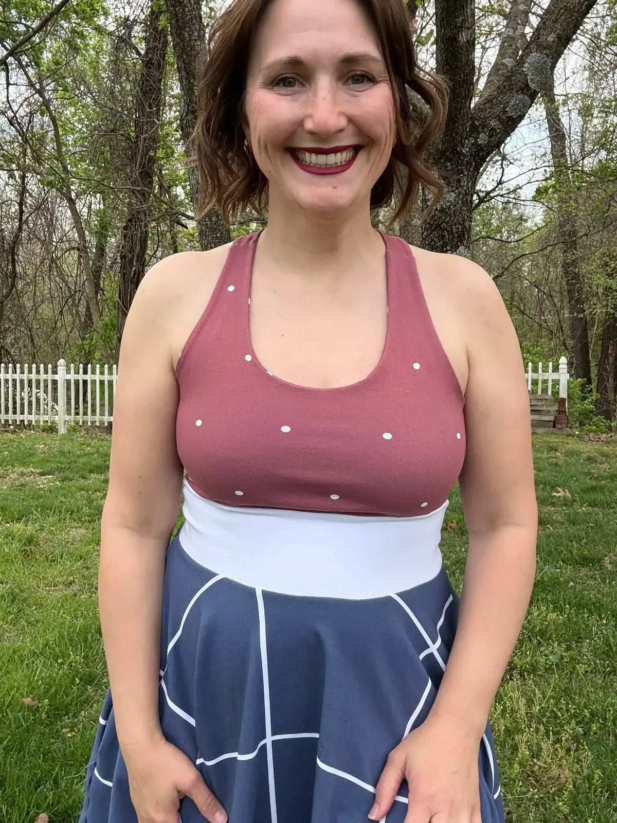 A woman wears a red polka dot top and a blue and white patterned skirt.