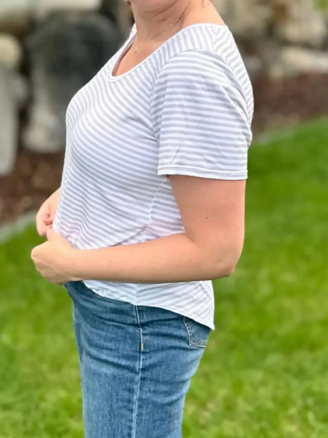 A woman wears a white and tan striped short-sleeved shirt and blue jeans.
