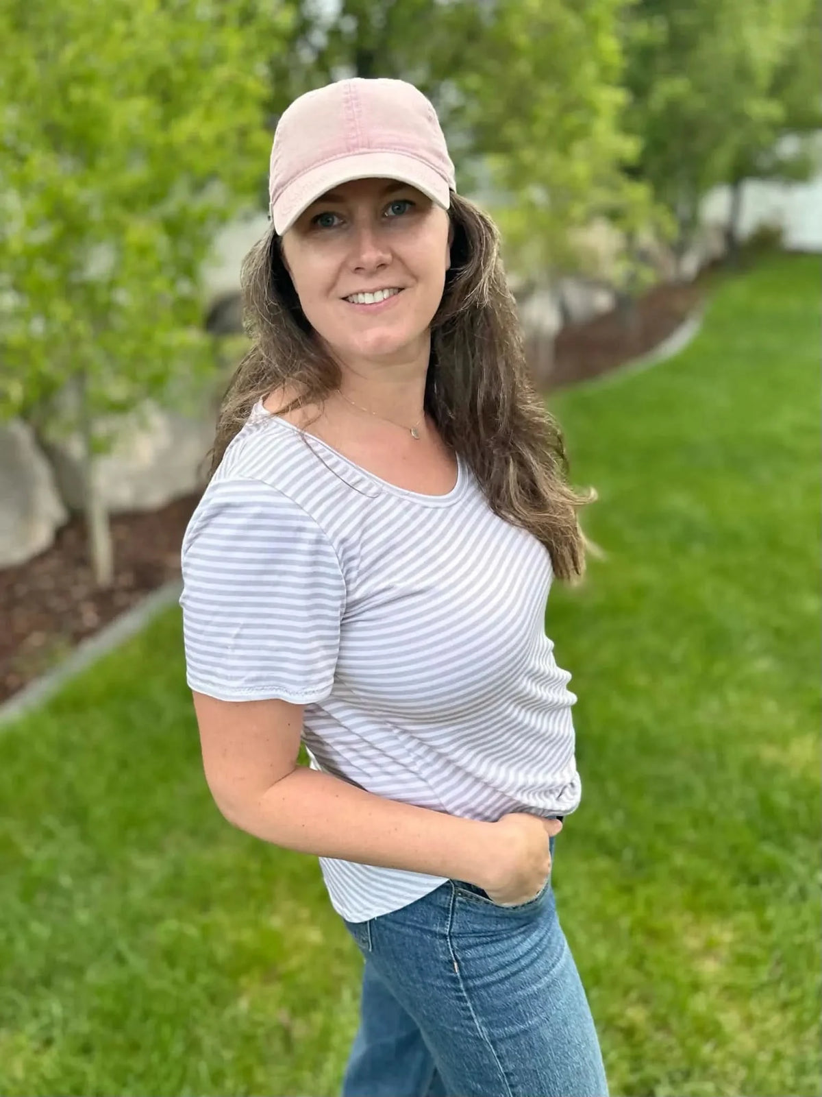 A woman in a tan and white striped shirt and jeans smiles at the camera.