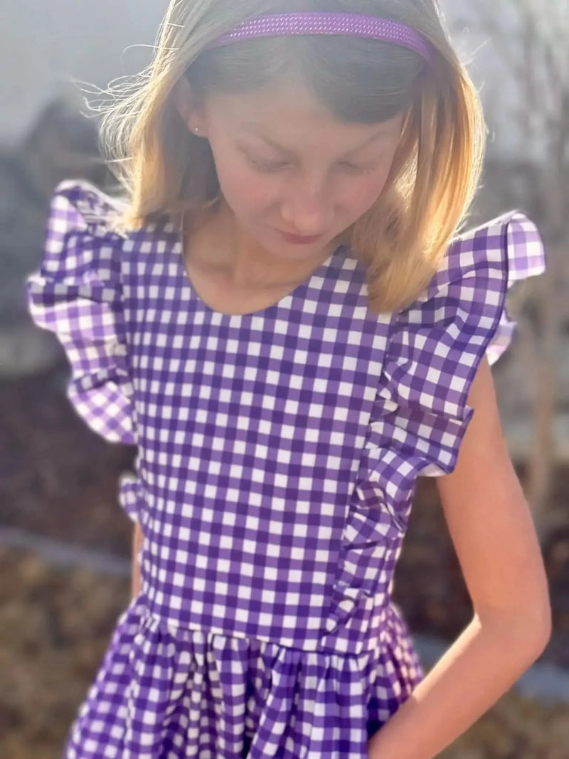 A young girl wears a violet and white gingham dress with ruffled sleeves.