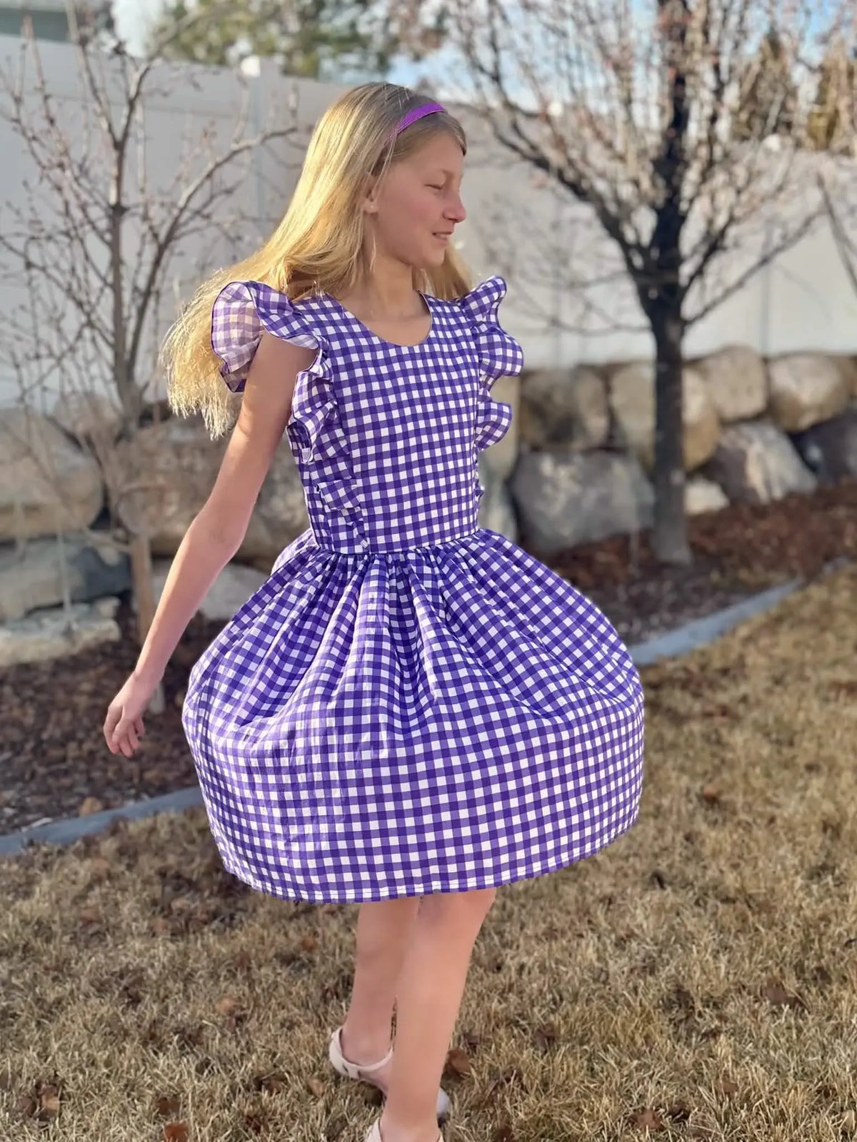 A girl in a purple and white gingham dress with ruffled sleeves.