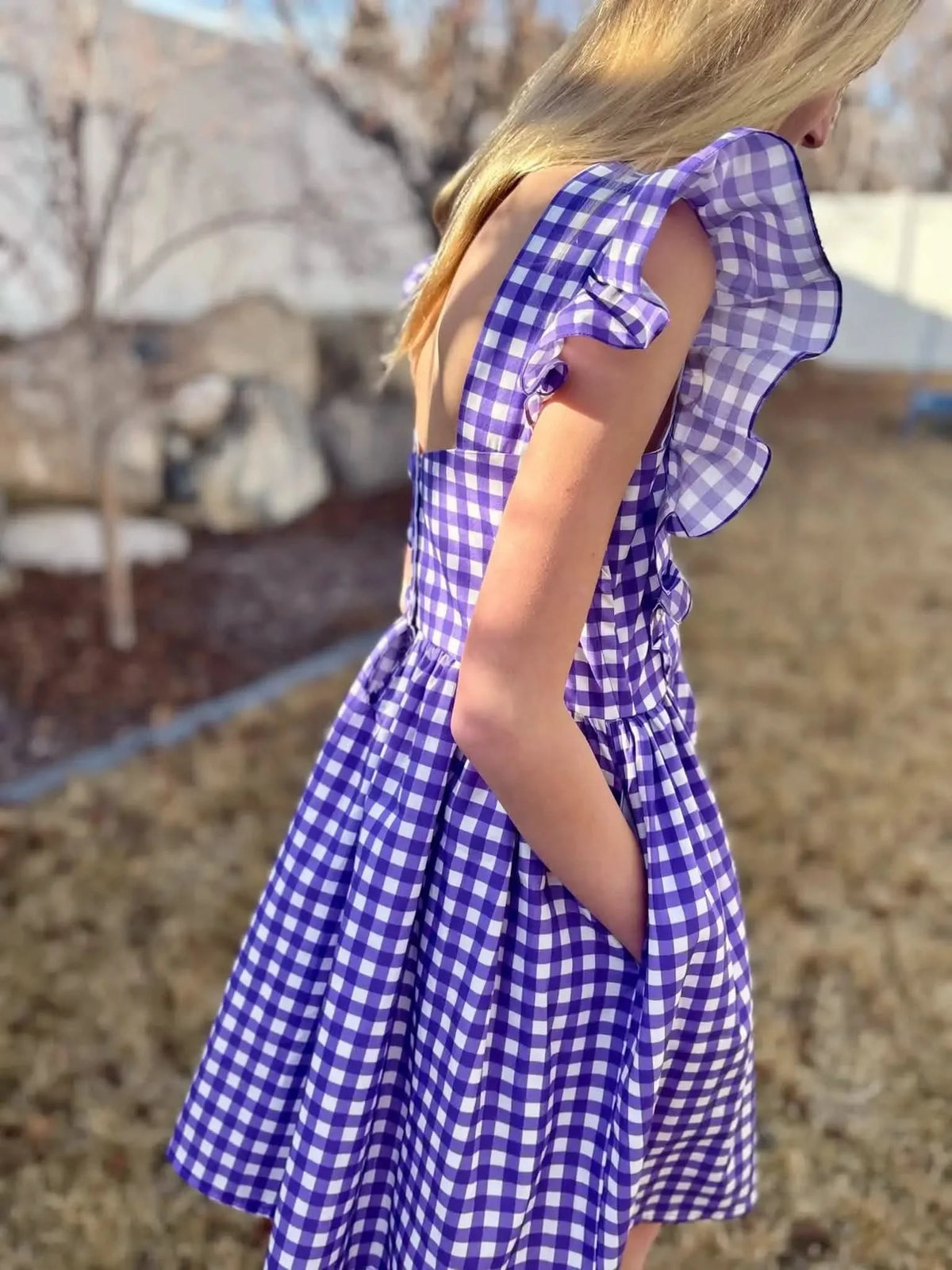 A person wearing a violet and white gingham dress with ruffled sleeves and pockets.