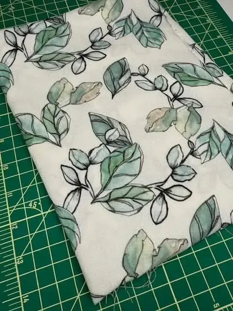 Fabric with a white background and a pattern of green and brown leaves.