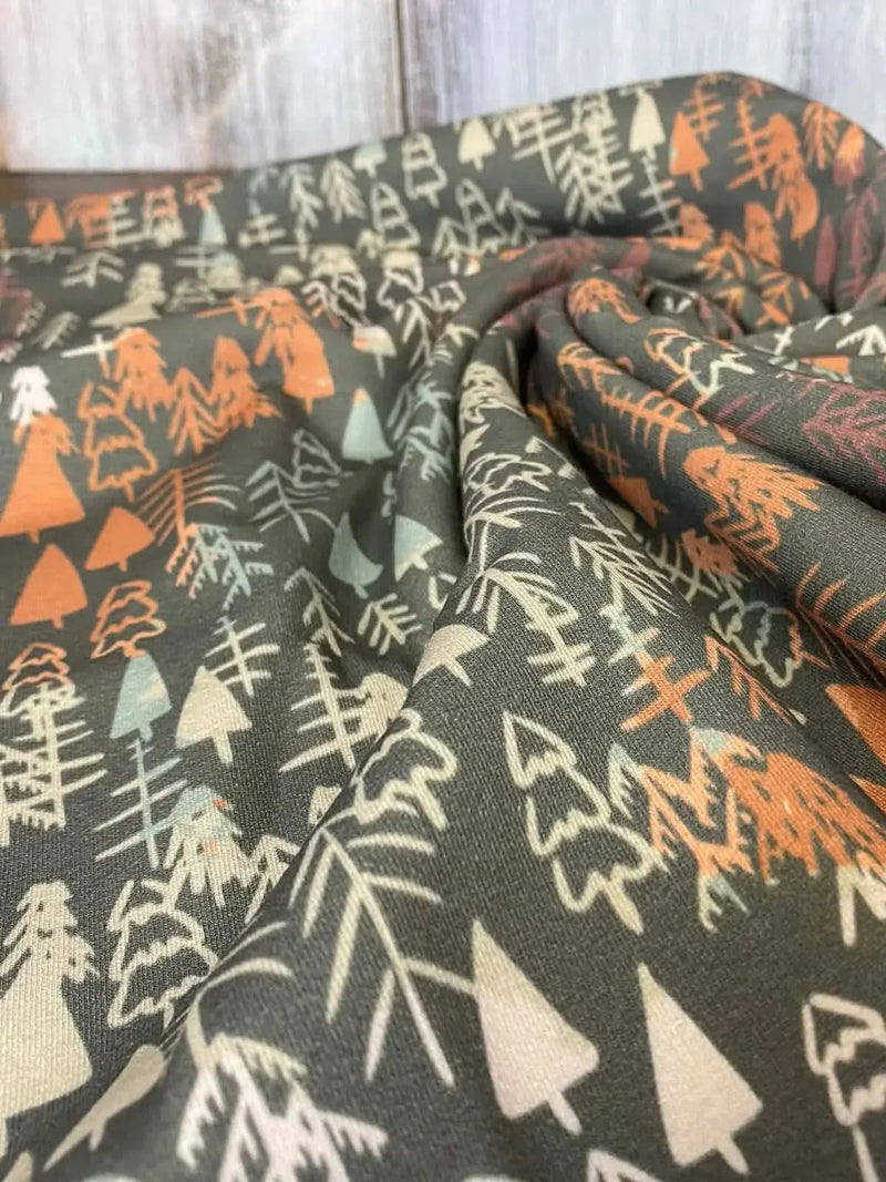 Dark fabric with a pattern of various trees in fall colors.