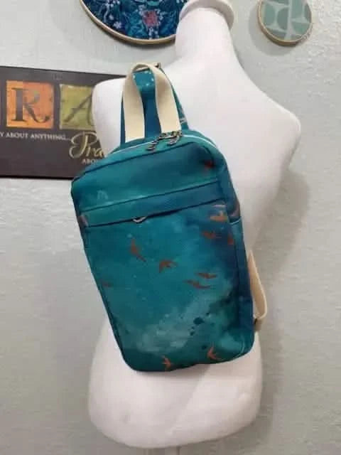 Dark teal sling bag with orange bird silhouettes on a white mannequin.