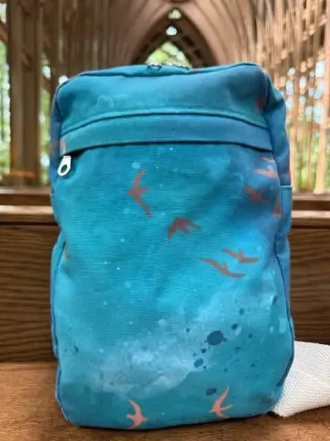 A dark teal bag with a sunset flight bird pattern and a zippered front pocket.