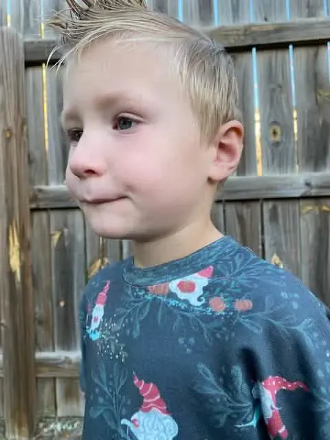 A young child wears a green shirt with a gnome toile pattern.