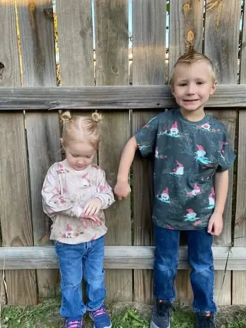 Two children wear gnome toile shirts, one in green and one in beige.